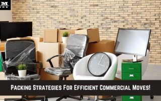 Office chairs, a desk, a monitor, a clock, and several cardboard boxes are arranged in front of a brick wall, suggesting a commercial move.